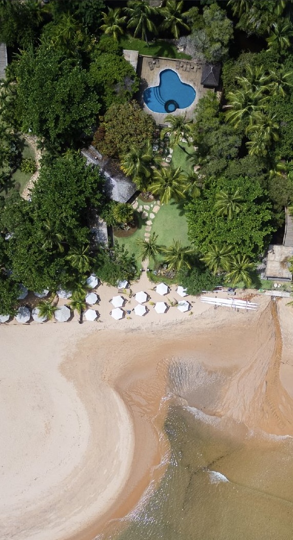 Vista aérea do UAU Beach Club, com piscina, jardim e área de praia com guarda-sóis