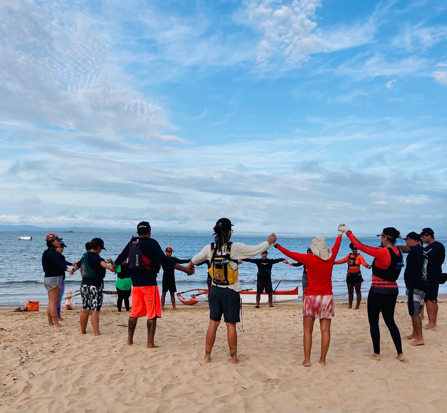 Grupo de mãos unidas na praia antes da remada, formando uma corrente humana