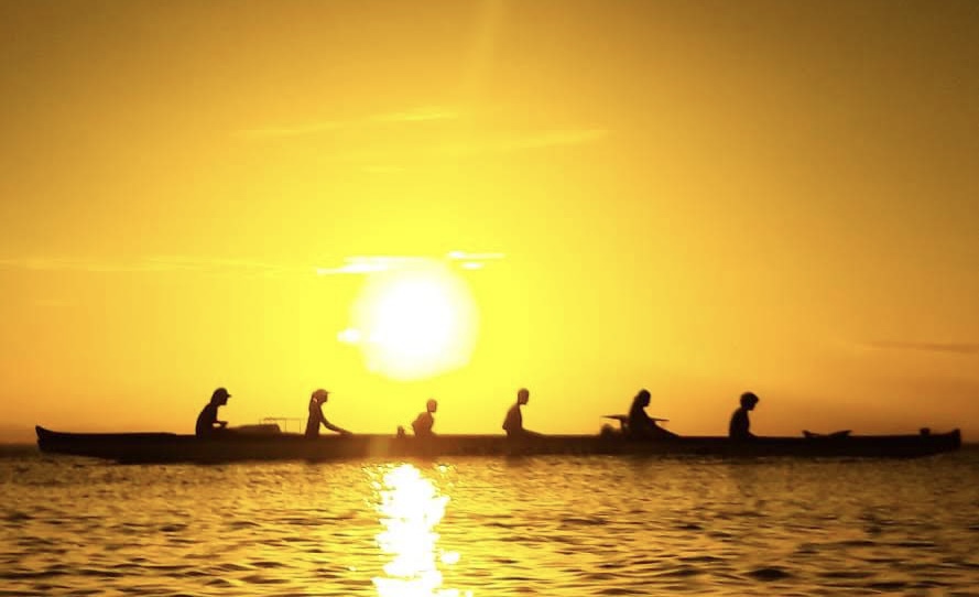 Tripulação em silhueta remando contra o pôr do sol dourado