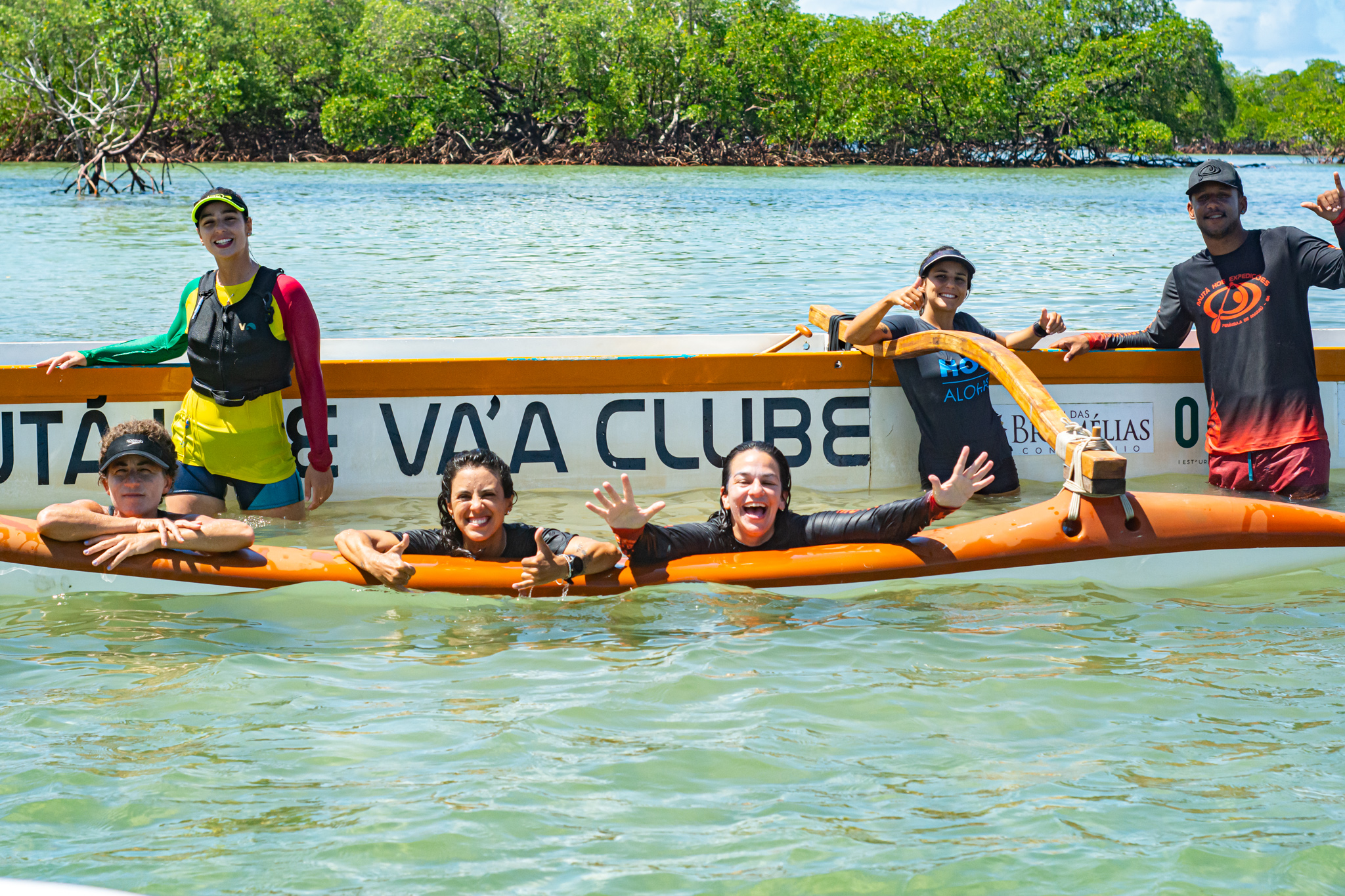 Grupo sorridente na água, unido ao redor da canoa do clube